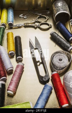 Una teglia piena di accessori per cucire con un metro a nastro e bobine di filo in vari colori, forbici, aghi e spille di sicurezza Foto Stock