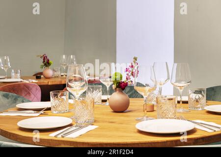 Tavoli da pranzo rotondi in legno di un ristorante con vetreria accanto ai piatti e alcune piante decorative Foto Stock