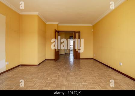 Una grande camera vuota con pavimenti in parquet di quercia disposti a scacchiera e una doppia porta di accesso in legno di sapele con finestre Foto Stock