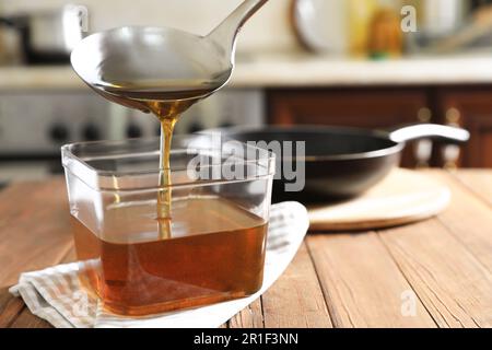 Versare l'olio da cucina usato con il mestolo nel contenitore sul tavolo di legno in cucina Foto Stock