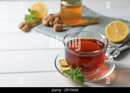 Tazza di delizioso tè allo zenzero e ingredienti su un tavolo di legno bianco, spazio per il testo Foto Stock