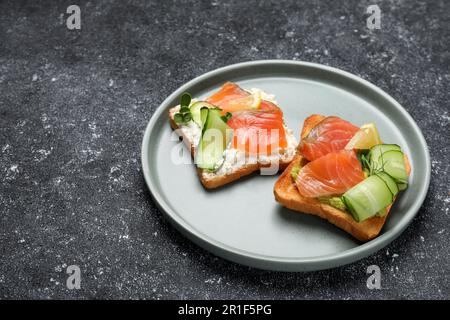 Toast gustosi con salmone, formaggio cremoso e cetriolo sul tavolo grigio Foto Stock