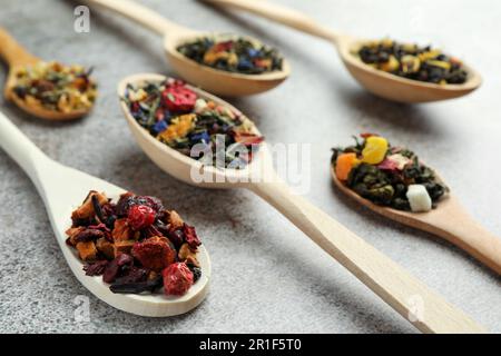Diversi tipi di tisana secca in cucchiai di legno su tavolo grigio chiaro, primo piano Foto Stock