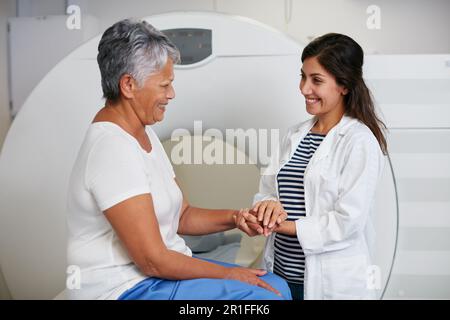 Medico, scansione tc e donna che tiene le mani del paziente in ospedale prima di eseguire la scansione sulla macchina. MRI, comfort e felice medico professionale con senior Foto Stock