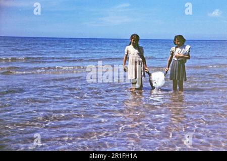 Due giovani ragazze in piedi in acqua, tenendo un pesce luna (o pesce Opah) che è stato utilizzato per fare sapone ca. 1950-1955 Foto Stock