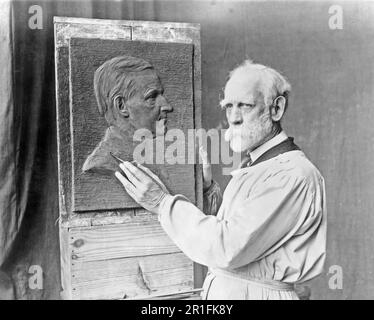 Foto di archivio: Henry K. Bush-Brown, ritratto a metà lunghezza, indossare smock e lavorare al suo ritratto a bassorilievo di Calvin Coolidge ca. 1925 Foto Stock