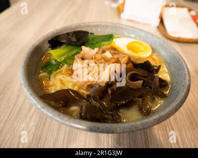 Una ciotola di ramen che consiste di uovo, fungo, tagliatelle e verdure, su un tavolo di legno Foto Stock