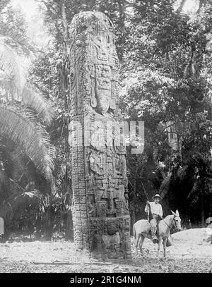 Foto di archivio: Uomo su un cavallo accanto a un monumento in pietra a Quiriguá, un antico sito archeologico Maya in Guatemala ca. 1908-1919 Foto Stock