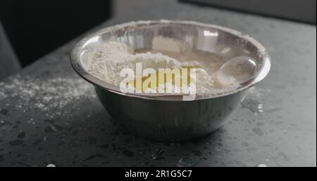 inumidire gli ingredienti nella farina in una ciotola d'acciaio sul piano di appoggio in calcestruzzo, foto ampia Foto Stock