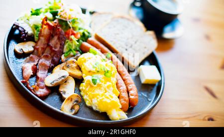 Colazione con uova strapazzate, pancetta, salsicce e toast sul tavolo del ristorante Foto Stock
