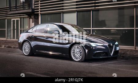 Un'auto Alfa Romeo argentata parcheggiata accanto a un edificio in cemento e a un marciapiede Foto Stock