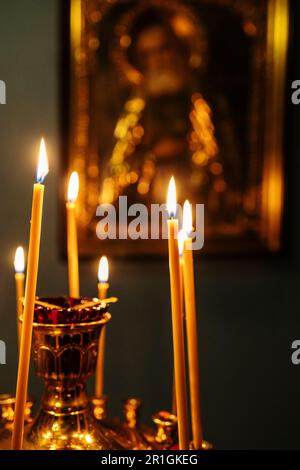 candele funebri bruciano sull'altare di fronte all'icona nella chiesa scura Foto Stock