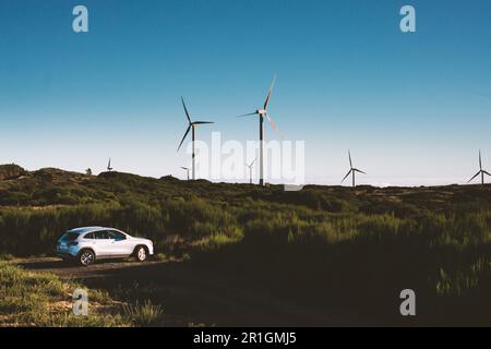 Auto elettrica parcheggiata nel campo vicino alle turbine High Wind all'esterno Foto Stock