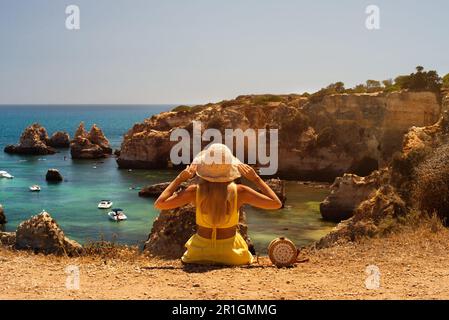 Vista posteriore della signora seduta sulla scogliera guardando l'oceano Foto Stock