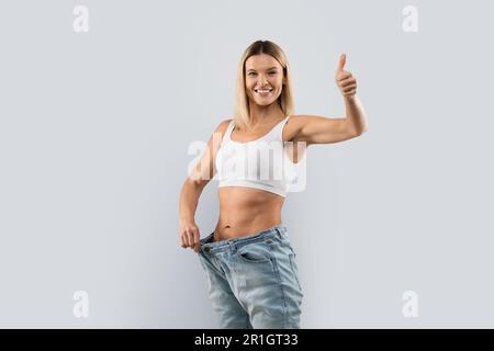 Donna felice di mezza età che indossa jeans grandi mostrando pollice in su Foto Stock