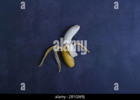 Banana parzialmente sbucciata su sfondo blu scuro. Vista dall'alto. Spazio di copia Foto Stock
