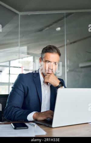 Un uomo d'affari serio di mezza età, ceo seduto alla scrivania, che utilizza il pensiero di un notebook. Foto Stock