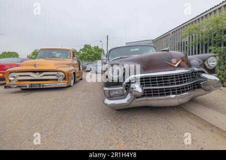 Rayleigh, Regno Unito. 14 maggio 2023. Una Cadillac nera intemprata e un pick-up Ford giallo-oro lucido parcheggiato su un'altura di ghiaia a Rayleigh, Essex. La scena rievoca l'americana della metà del secolo in uno sfondo suburbano britannico. Camion Farm Fresh Garage e veicoli americani in mostra. Penelope Barritt/Alamy Live News Foto Stock