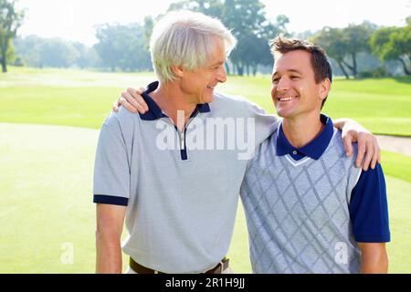 Padre e figlio sorridono e si guardano l'un l'altro. Ritratto di padre e figlio sul campo da golf sorridendo e guardandosi l'un l'altro. Foto Stock