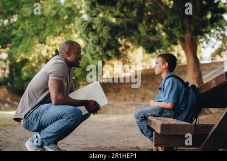 Mentore che parla con un giovane bambino di scuola fuori classe. Insegnante di scuola elementare che motiva un giovane ragazzo. Insegnante che fornisce supporto e incoraggiamento per un p Foto Stock