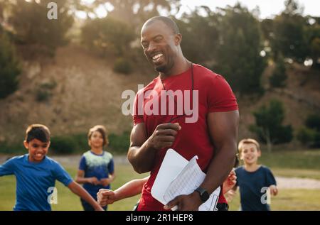 Allenati con i bambini in una scuola per una sessione di allenamento divertente. Insegnante di PE che istruisce un gruppo di bambini della scuola elementare. Educazione sportiva in sco elementare Foto Stock