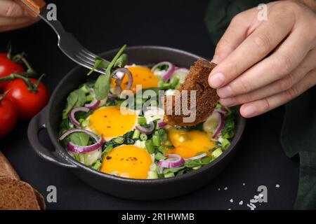 Donna che tuffa il pezzo di pane in tuorlo d'uovo, primo piano. Mangiare gustoso Shakshuka Foto Stock