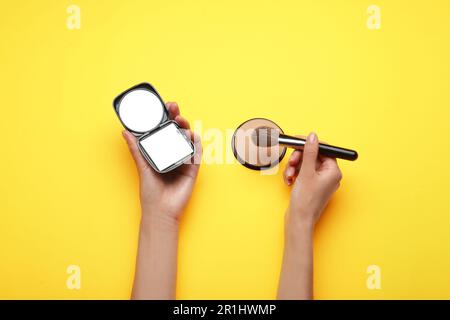 Donna che tiene uno specchio da tasca e una spazzola su sfondo giallo, vista dall'alto Foto Stock