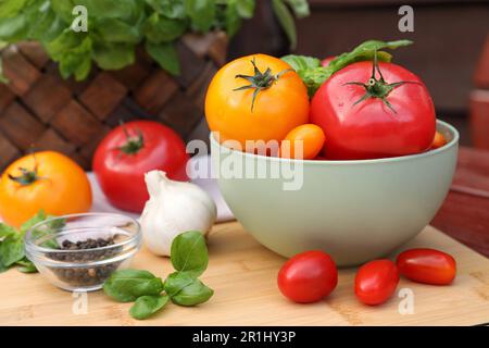 Diversi tipi di pomodori con basilico e pepe su tavola di legno Foto Stock