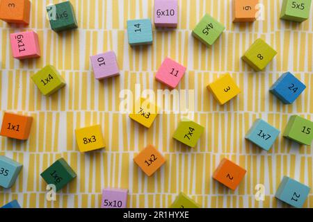 Cubi colorati con numeri e moltiplicazioni su sfondo giallo, piatto Foto Stock