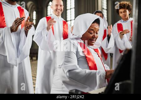 Gruppo di persone dal coro della chiesa in costume bianco cantando e suonando pianoforte in chiesa Foto Stock