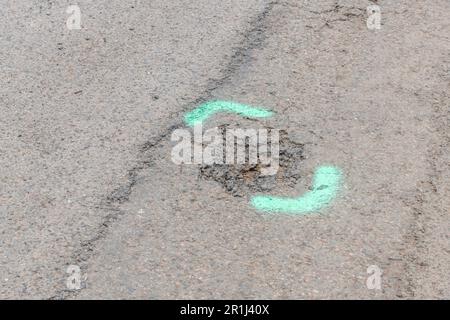 Segnaletica verde verniciata a spruzzo su strada asfaltata. Per le riparazioni su strada nel Regno Unito, concetto di manutenzione, con metafora sottile. Foto Stock