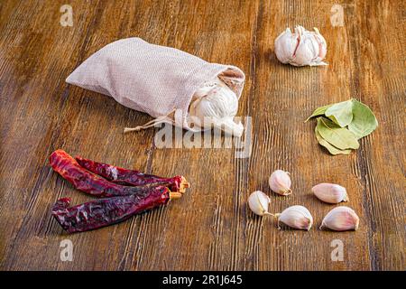 Un tavolo di legno con un sacchetto di stoffa riempito con spicchi d'aglio, peperoni secchi e foglie di alloro Foto Stock