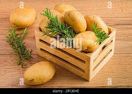 Una cassa di legno con patate e piante di erbe verdi su un tavolo di legno Foto Stock