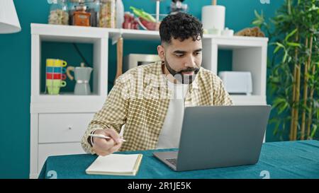 Giovane ispanico che usa il portatile per scrivere appunti in sala da pranzo Foto Stock