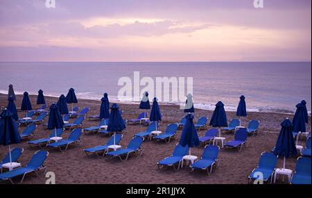 La costa marina dell'isola e una spiaggia attrezzata per i turisti con lettini e ombrelloni in fila e ponti di legno tra di lettini. Foto Stock