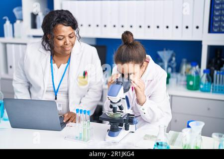 Madre e figlia scienziati che utilizzano microscopio e laptop che lavorano in laboratorio Foto Stock