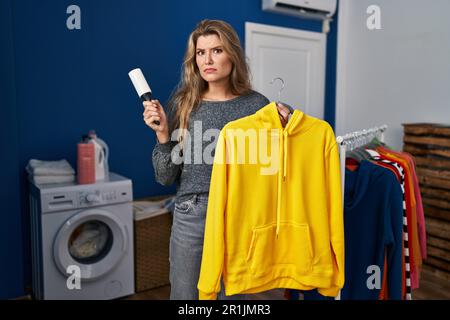 Giovane donna che usa il rotolo di lanugine per rimuovere i capelli dai vestiti espressione clueless e confusa. concetto di dubbio. Foto Stock