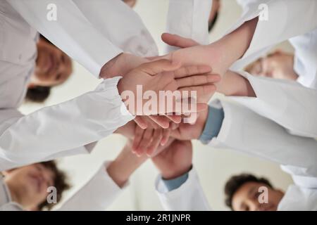 Primo piano dei bambini che si accatastano con le mani in classe scientifica e indossano camici da laboratorio bianchi Foto Stock