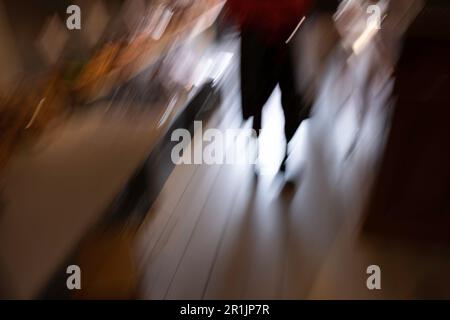 Vista astratta con sfocatura in movimento di una silhouette di una persona confusa su un pavimento in legno con retroilluminazione. Immagine di sfondo Foto Stock