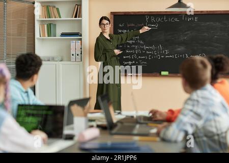 Ritratto della donna come insegnante di scienza femminile che scrive sulla lavagna in classe e guarda i bambini, copia spazio Foto Stock