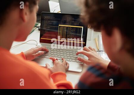 Vista posteriore a scolari che utilizzano il computer portatile in un corso di programmazione per i bambini a scuola Foto Stock