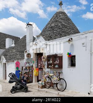 Bambini che giocano a flauti giocattolo di fronte al piccolo negozio di Rione Monti, Alberobello, Puglia Foto Stock