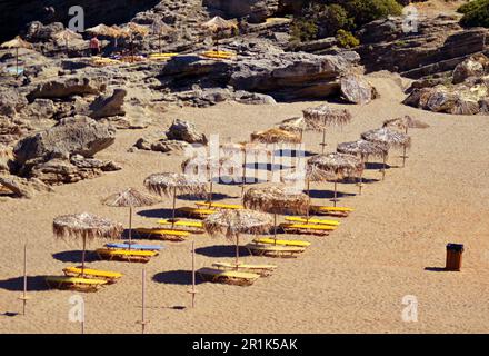 Spiaggia di sabbia con lettini e ombrelloni sul mare, sull'isola. Le sedie a sdraio sono gialle e blu. Ombrelloni di paglia accanto ai lettini Foto Stock