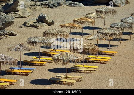 Spiaggia di sabbia con lettini e ombrelloni sul mare, sull'isola. Le sedie a sdraio sono gialle e blu. Ombrelloni di paglia accanto ai lettini Foto Stock