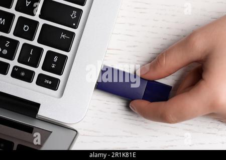 Donna che collega l'unità flash usb al computer portatile su un tavolo di legno bianco, vista dall'alto Foto Stock