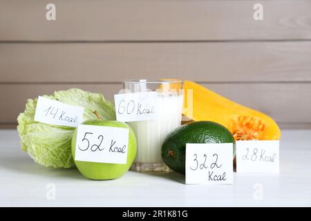 Prodotti alimentari con etichette di potere calorifico su tavola di legno bianco. Concetto di perdita del peso Foto Stock