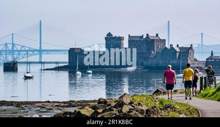 Persone che camminano sul sentiero costiero vicino al castello di Blackness con ponti a distanza, Scozia, Regno Unito Foto Stock