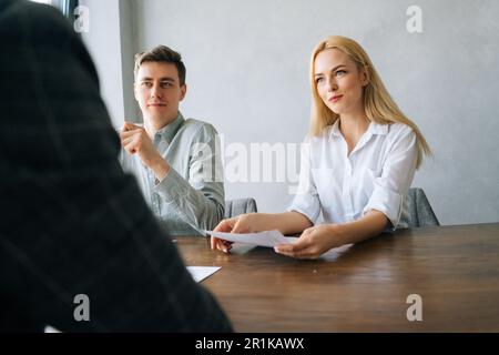 Vista posteriore di giovani e professionisti cacciatori di teste di uomo e donna che tengono un'intervista con irriconoscibile maschio cercatore di lavoro. I responsabili delle risorse umane caucasici hanno un lavoro Foto Stock