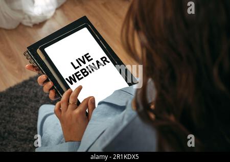 Concetto di apprendimento online. Una donna tiene in mano un tablet sullo schermo del quale è scritto - Webinar dal vivo Foto Stock