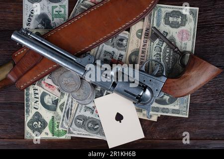 Vecchia arma occidentale. Colt Revolver, coltello asso di picche carta da gioco su carta e argento dollari cumulo sul ponte. Foto Stock